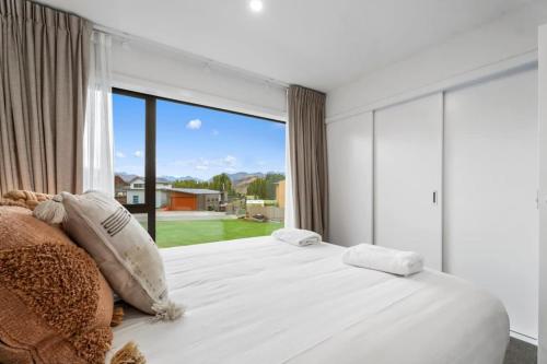 a bedroom with a large white bed with a large window at Wanaka Riverside Townhouse Retreat in Albert Town