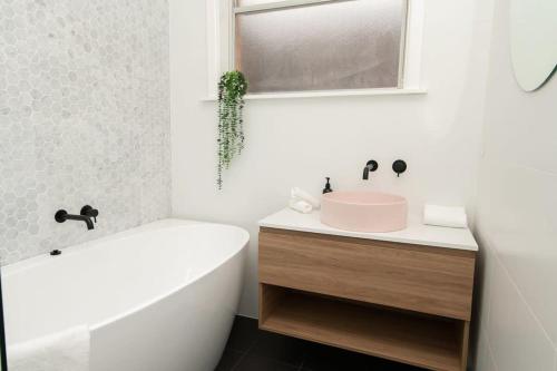 a bathroom with a white tub and a sink and a bath tubermott at Haven on Hill - Modern & Charming, Touch of Pink in Orange