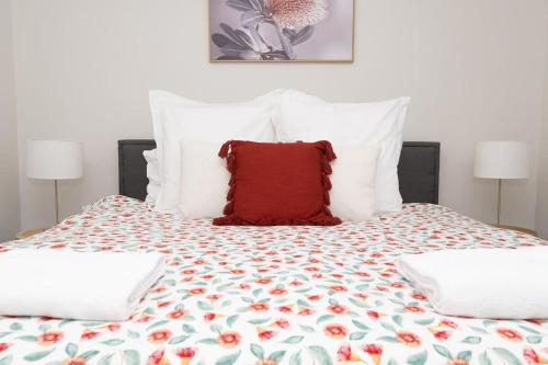 a bed with a red pillow on top of it at The Valerie Gardens - Homely & Cosy, Sleeps 11 in Orange