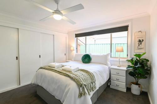 a white bedroom with a large bed with a ceiling fan at Aspen Abode - CBD, Fireplace, BBQ, 3 Smart TVs in Dubbo