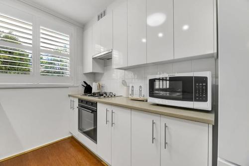 a white kitchen with white cabinets and a microwave at Hope St Cottage - Elegant & Cosy, Sleeps 6 in Bathurst