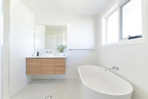 ein weißes Badezimmer mit einer Badewanne und einem Waschbecken in der Unterkunft Hideaway on Curran - CBD Escape, EV Plug, Firepit in Orange