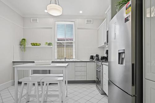 a white kitchen with a table and a refrigerator at Hamptons House - Scandi Heritage Charm in Bathurst