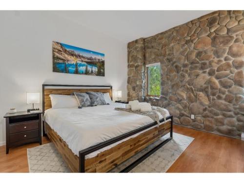1 dormitorio con 1 cama grande y pared de piedra en Chardonnay Chalet I Fireplace I Mountain View I TV en Invermere