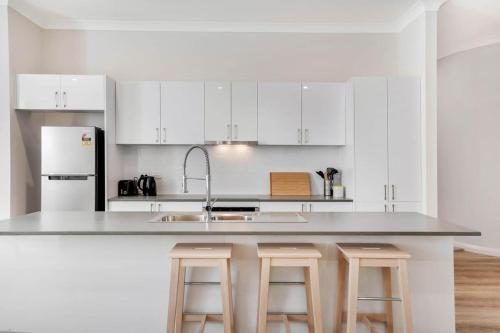 a kitchen with white cabinets and a counter with stools at Crooked Lane Apartment - CBD, Stylish & Central in Wagga Wagga