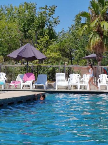 une personne nageant dans une piscine avec des chaises et un parasol dans l'établissement Mobilhome Confort en camping 4*, au Grau-du-Roi