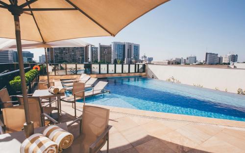 una piscina en la azotea de un edificio con sillas y sombrilla en Cullinan Hplus Premium Flat Vip en Brasilia