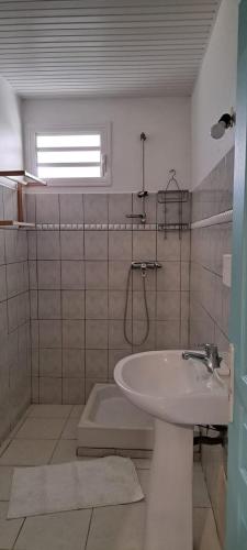 ein weißes Bad mit einem Waschbecken und einem Fenster in der Unterkunft Villa Léïna in Le Robert