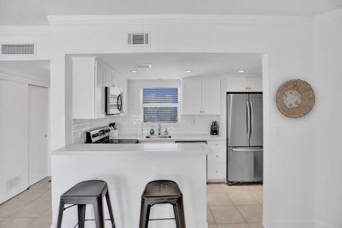eine weiße Küche mit zwei Barhockern und einem Kühlschrank in der Unterkunft Fort Lauderdale Yacht & Beach Club 412 in Fort Lauderdale