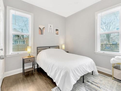 a white bedroom with a bed and two windows at Cozy Home Near Downtown Detroit in Detroit