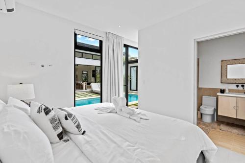 a white bedroom with a white bed and a bathroom at Modern Garden Villa with Private Pool, Outdoor Kitchen & Separate Casita Near Playa Potrero in Potrero