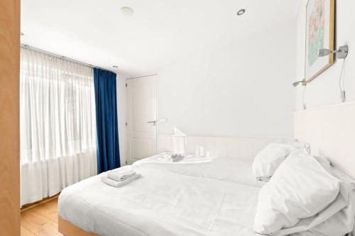 a white bedroom with two beds and a window at Hello Zeeland - Vakantiehuis Zuidstraat 17A in Domburg