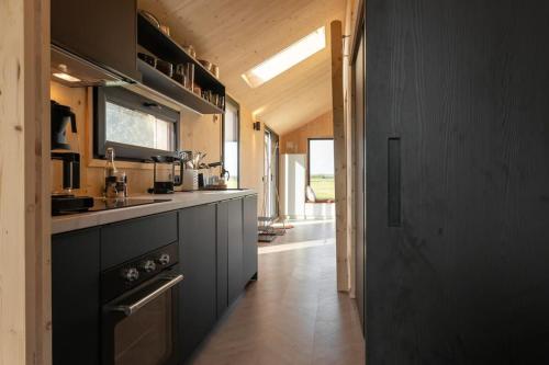 een grote keuken met zwarte kasten en een hal bij Hello Zeeland - Zeeuwse Liefde Tiny House 8 in Westkapelle