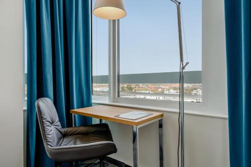 a desk with a chair and a lamp and a window at Motel One München-Campus in Munich