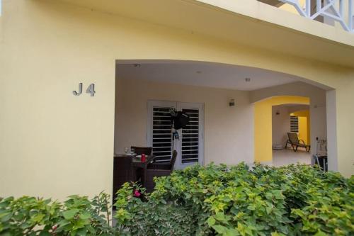 une maison blanche avec un porche avec une haie dans l'établissement Caracara J4 Relax & Dive Resort Bonaire Village, à Kralendijk