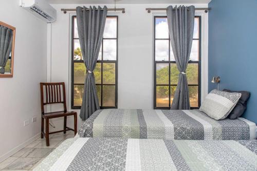 a bedroom with two beds and a chair and windows at Caribbean Court Apartment Good Vibes in Kralendijk
