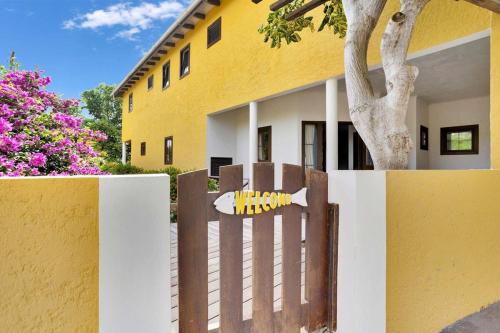 a fence in front of a yellow building with a tree at Villa Kromboon with an amazing sea view in Kralendijk