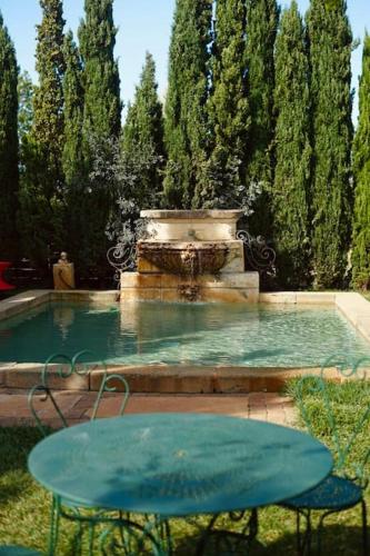 une fontaine avec une table bleue et des chaises devant dans l'établissement Grande Maison de Charme a 5 mn du centre ville, à Narbonne