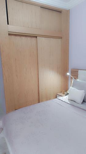a bedroom with a white bed with a wooden door at Appartement Basatine in Fès