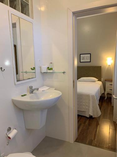 baño con lavabo, espejo y cama en Hotel Jardim Bulevard, en Ituporanga