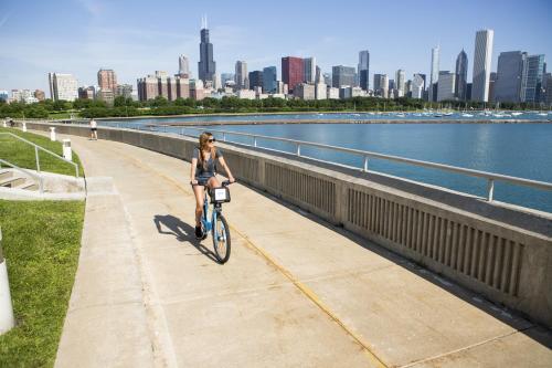 a woman riding a bike on a sidewalk near the water at HI Chicago Hostel in Chicago