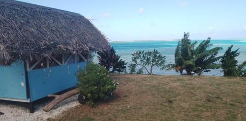a blue hut with a thatched roof and trees and the ocean at Taria camping in Te-Fare-Arii