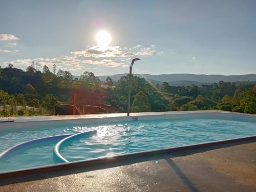 una piscina con el sol en el fondo en Sítio Âmbar - Família, tranquilidade e privacidade, en Lambari