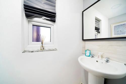 een witte badkamer met een wastafel en een spiegel bij Chic 4BR Home with Ensuite bath and Cozy Garden in Dagenham