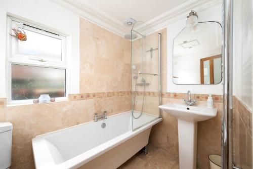 ein Badezimmer mit einer Badewanne, einem Waschbecken und einem Spiegel in der Unterkunft Charming 2BR Home with Garden in Twickenham