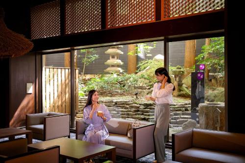 Dos mujeres en kimonos parados en una habitación en Ooedo Onsen Monogatari Premium Yamashitaya, en Kaga