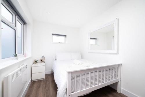a white bedroom with a crib and a mirror at Cozy single level flat with parking in Enfield