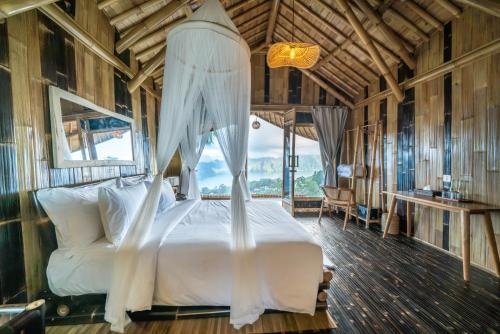 The Dewi Eco Bamboo Villa في كوبوبانلوكان: غرفة نوم بسرير أبيض في غرفة بها نوافذ