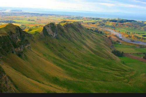 a green hillside with a river in the distance at Soak in Cedar Tub, Stroll to Havelock Village in Havelock North