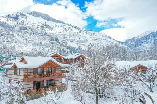 a log cabin in the snow with mountains in the background at Storii By ITC Hotels Urvashis Retreat, Manali in Manāli