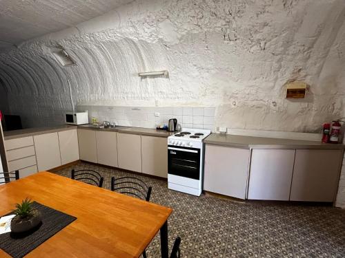 cocina con armarios blancos, mesa y fogones en Desert View Apartments, en Coober Pedy
