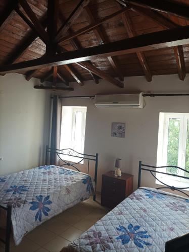 two beds in a room with wooden ceilings and windows at Villa Fraoulitsa in Skoutarion