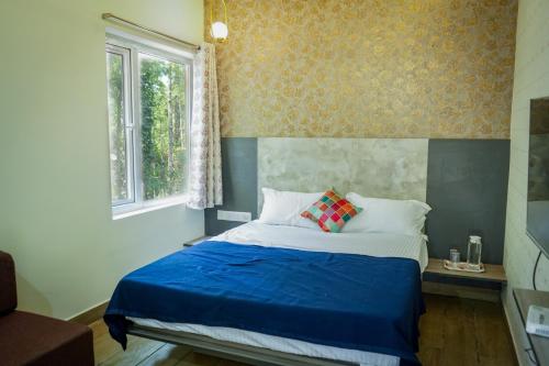 a bedroom with a bed with blue sheets and a window at Hotel Alpenglow in Yercaud