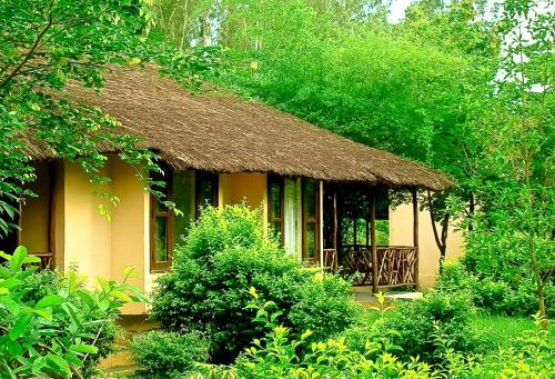 a small yellow house with a thatched roof at Jim's Jungle Retreat in Rāmnagar