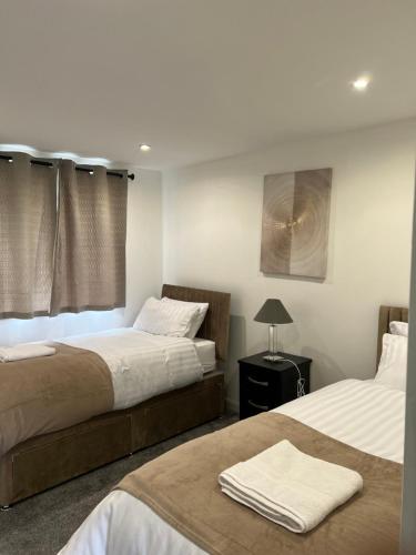 a bedroom with two beds and a table with a lamp at Majestic 2 bedroom House Milton Keynes in Milton Keynes