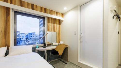 a bedroom with a bed and a desk and a window at Tabist MEN‘TEL Kitami in Kitami
