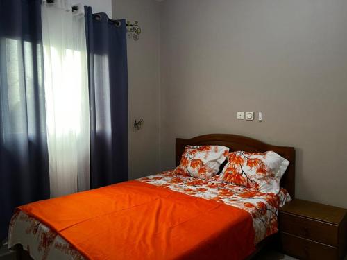 a bedroom with a bed with an orange blanket and a window at Magistral apparts in Yaoundé