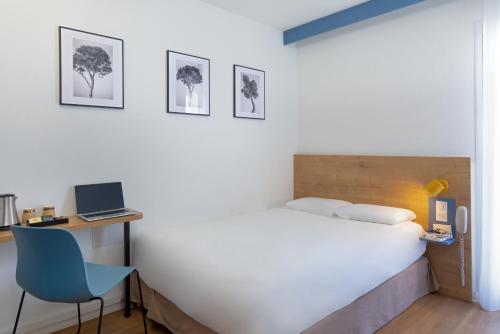 a bedroom with a bed and a desk with a laptop at KYRIAD MARSEILLE EST - Aubagne Gémenos in Gémenos