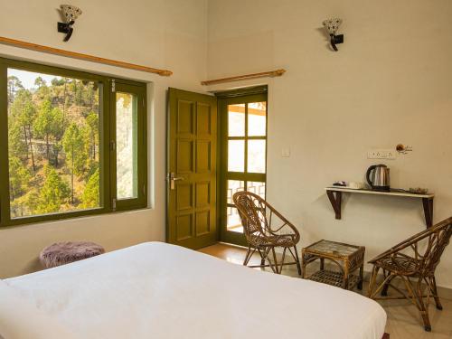 a bedroom with a bed and chairs and a window at THEHIMALAYANLIVING WHISTLING PINES in Mukteswar