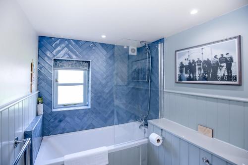 baño con paredes de azulejos azules y ventana en Pass The Keys Wilf's Barn, Wedmore a romantic cottage for two, en Wedmore