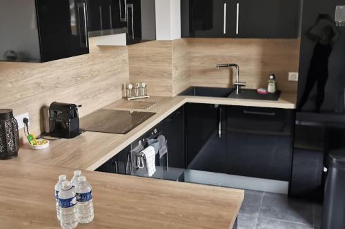 une cuisine avec des armoires noires, un évier et des bouteilles d'eau dans l'établissement Appartement près de Versailles - magnifique vue, à Fontenay-le-Fleury