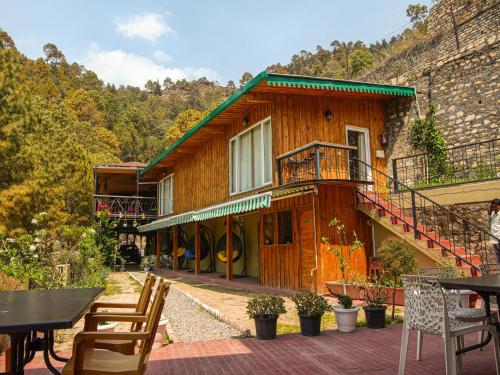 a wooden house with a balcony and tables and chairs at THEHIMALAYANLIVING WHISTLING PINES in Mukteswar