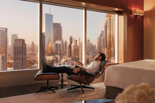 un hombre sentado en una silla en una habitación de hotel con una ventana en Jumeirah Emirates Towers Dubai, en Dubái