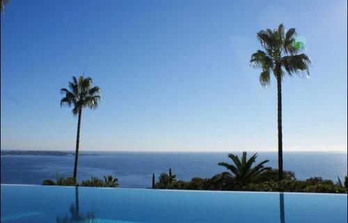 une piscine avec des palmiers et l'océan dans l'établissement Appart 2P Vue Mer Panoramique Cannes Eden, à Vallauris
