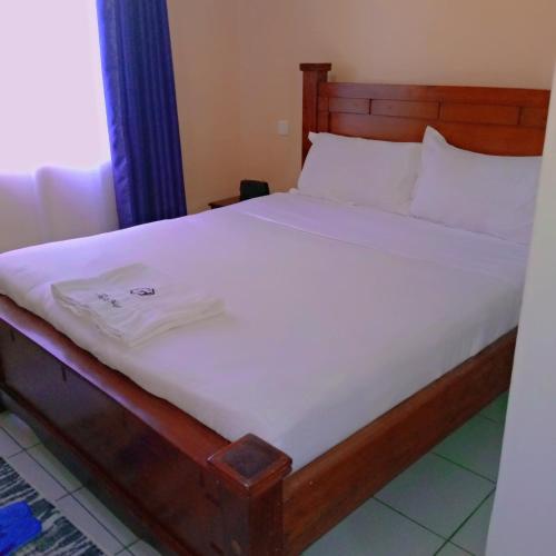 een bed met een houten frame en witte lakens bij New Carnation Pangani Hotel in Nairobi