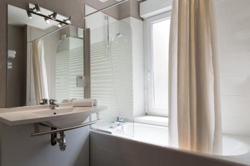 a bathroom with a sink and a tub and a window at The Originals Access, Hôtel Arum, Remiremont (Inter-Hotel) in Remiremont